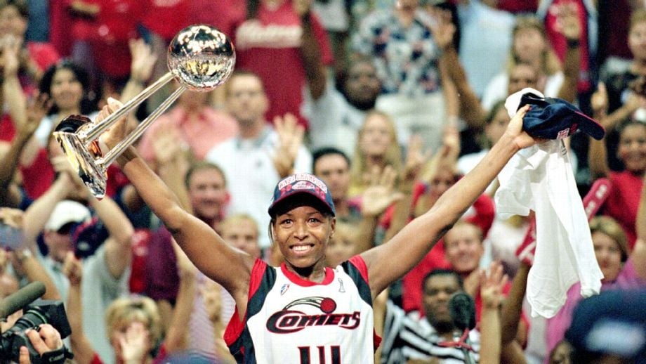 image shows WNBA icon Cynthia Cooper in her Houston Comets uniform, holding her Finals MVP trophy proudly in the air.
